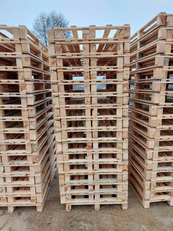 Fotografija stoga drvenih paleta u obliku piramide na parceli prekrivenoj zemljom.